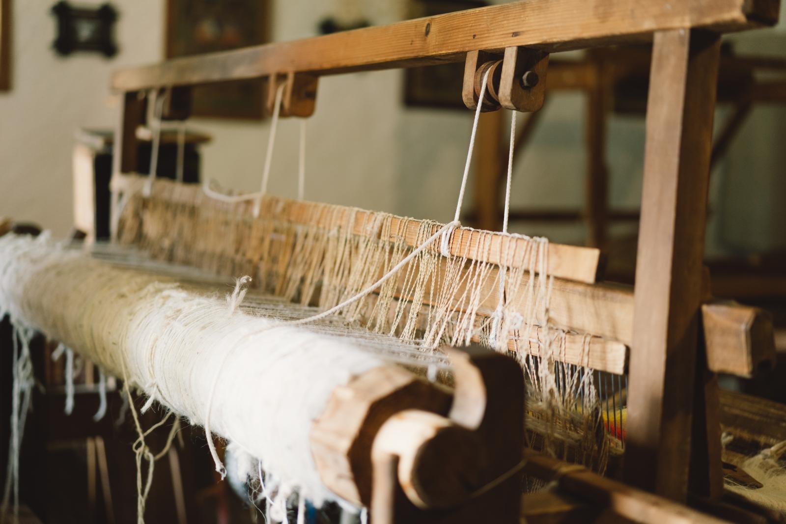 Threads run through an old wooden hand loom mid-weave.